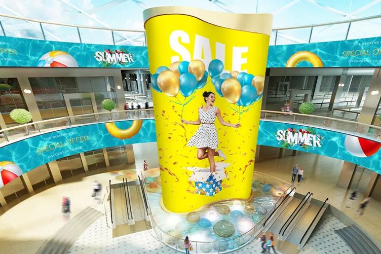 Shopping mall interior with large summer sale advertisement featuring balloons and a woman in a polka-dot dress.