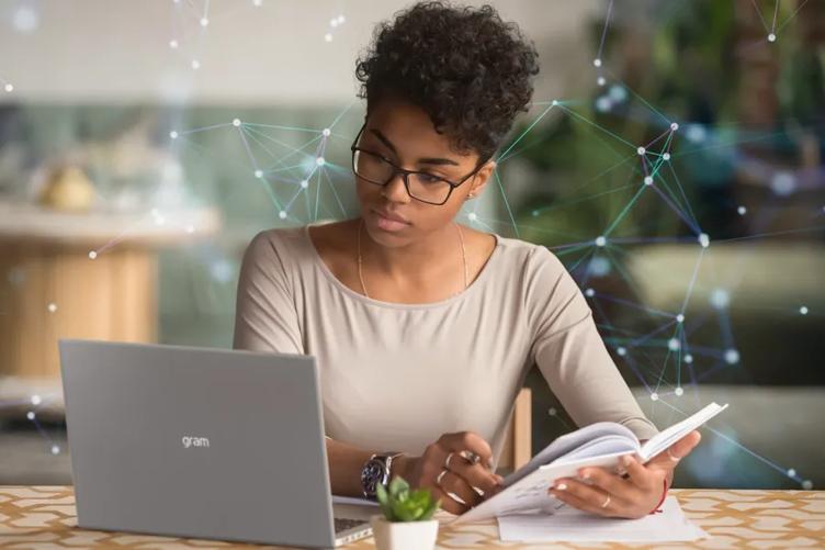 A woman sitting at a desk, using an LG Cloud mobile thin client gram laptop. She's looking at the display and writing something in a notebook. Behind her, green glowing dots connected by lines represent a digitally connected network. 
