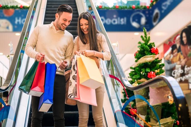 A couple smile as they descend an escalator in a shopping mall decorated for the holidays. Behind them, LG digital signage advertises holiday shopping deals.