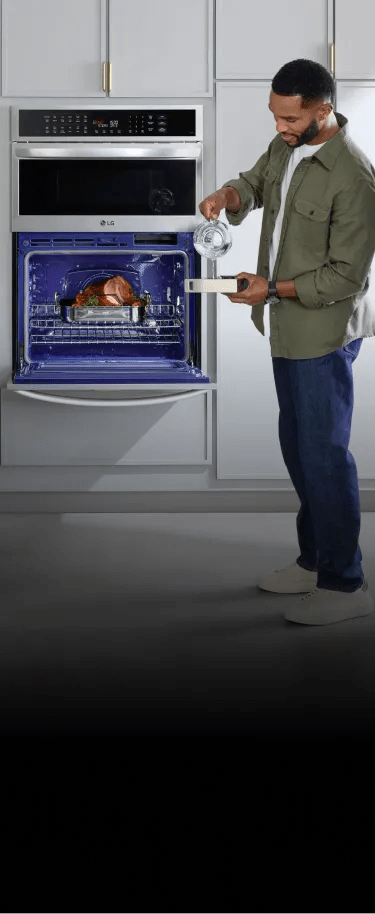 A mother slicing oranges for her daughter at the kitchen island while the father cooks a ham in their LG wall oven - mobile