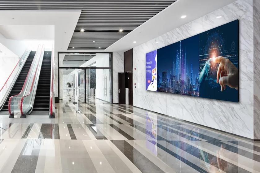 Modern building lobby with escalators and digital displays on the wall.