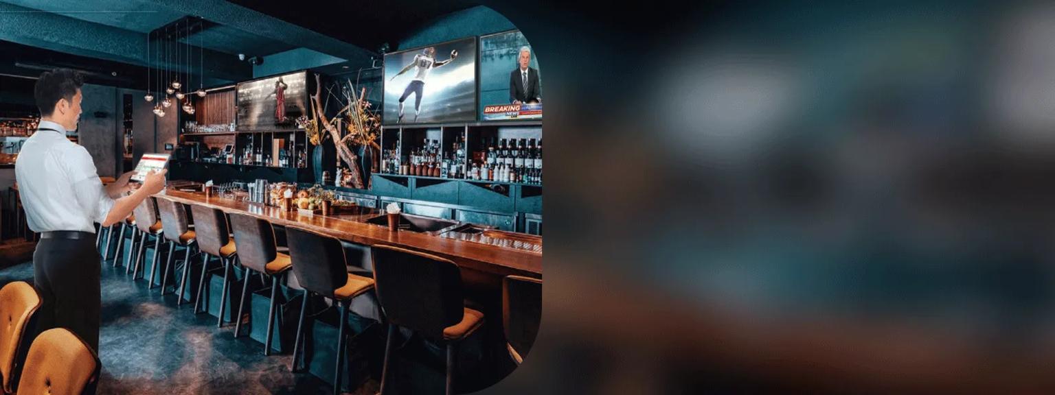 A restaurant manager using a tablet to connect with the LG displays and Pro:Centric Catena in his bar space