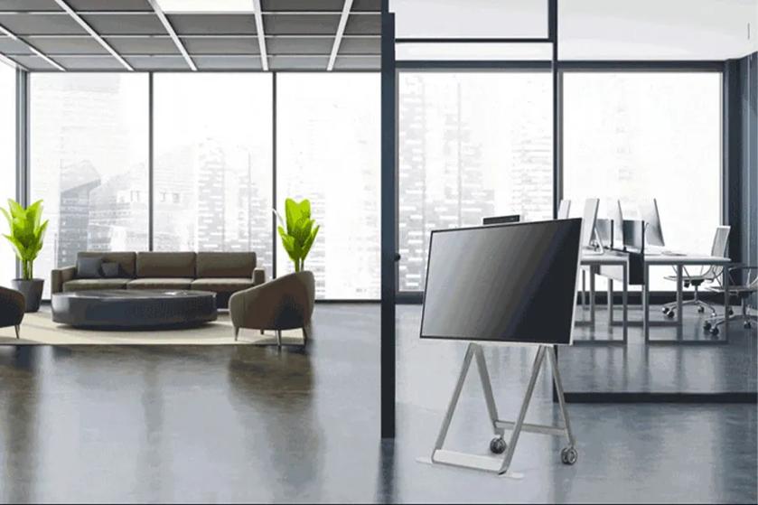 A One:Quick Flex stands in an open floorplan office, ready to be moved wherever it's needed thanks to its wheeled stand.