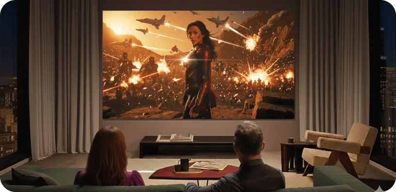 LG Ultra-Large TV displaying an action movie scene with a female hero amid sparks and debris, as two people sit on a couch watching in a modern living room.