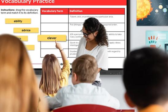 A teacher and student stand in front of a classroom, using an LG CreateBoard for a vocabulary lesson.