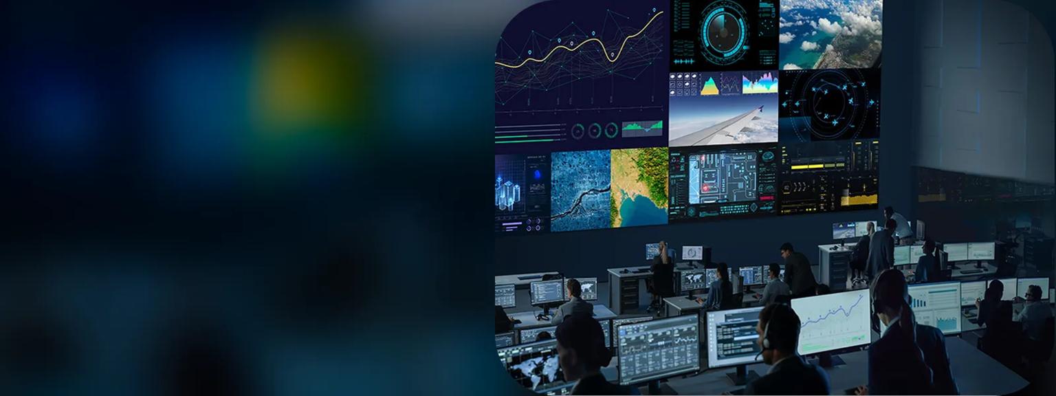 Mission control room with large digital signage video wall and desks full of brightly lit monitors