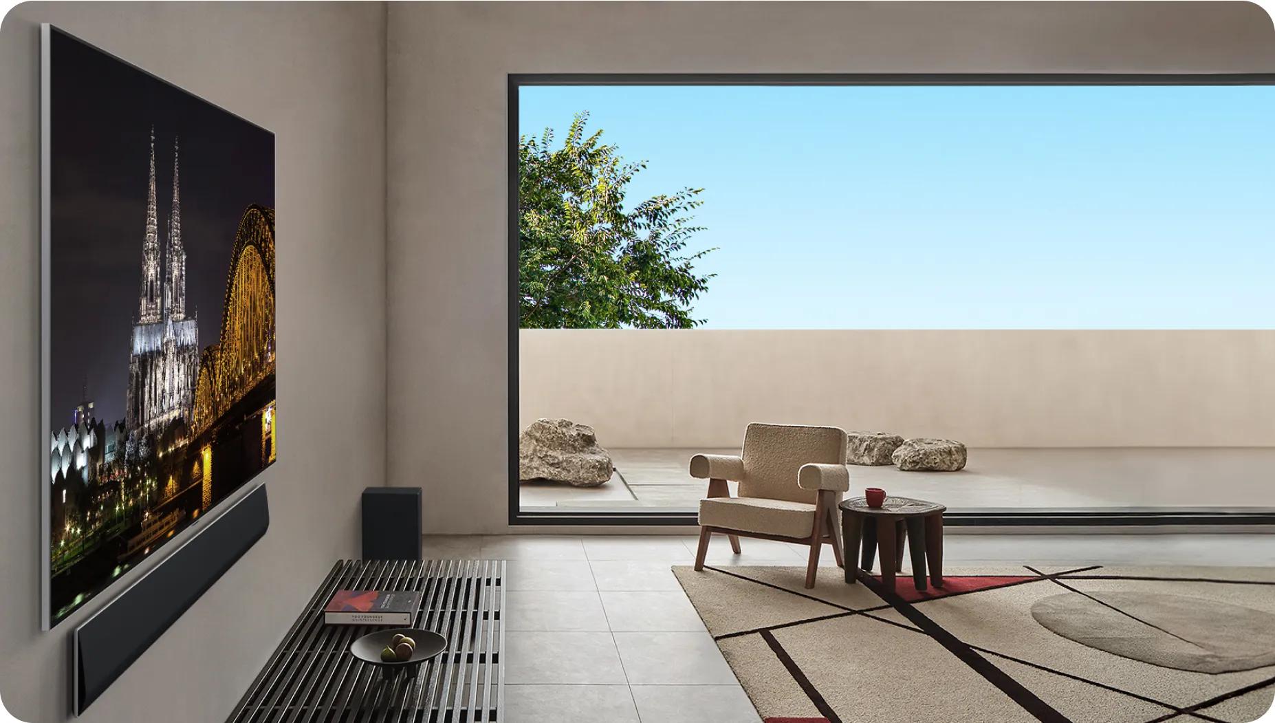 Minimal living room with a balcony and a very slim LG TV and soundbar mounted on the wall showing an illuminated cathedral and bridge at night.