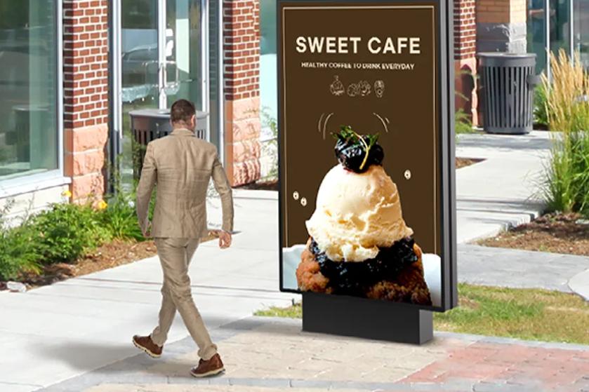 A man in a light brown suit walks past a digital ad featuring a dessert with ice cream on a city sidewalk.