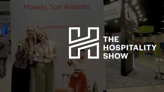 A photo of two women standing in front of LG's booth at The Hospitality Show 2024, darkened and with The Hospitality Show logo in white over it.