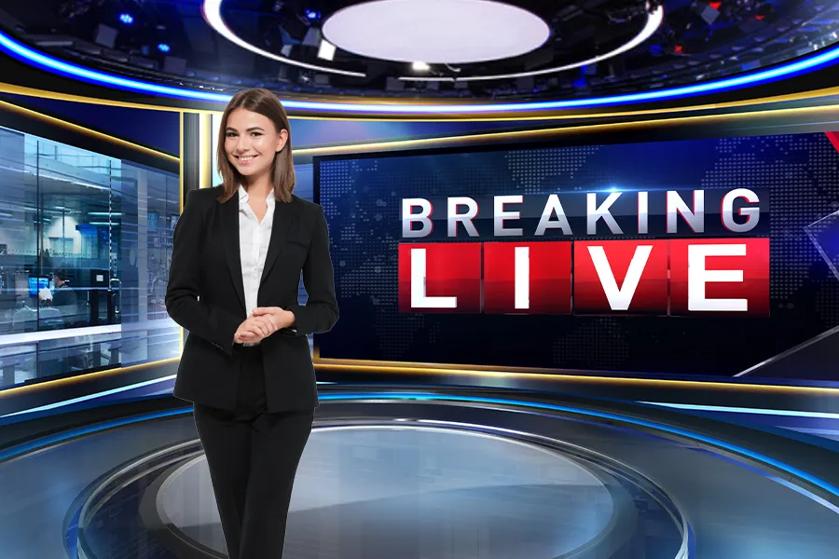 A newscaster stands in a studio, in front of a DVLED display with a Breaking: Live graphic on it.