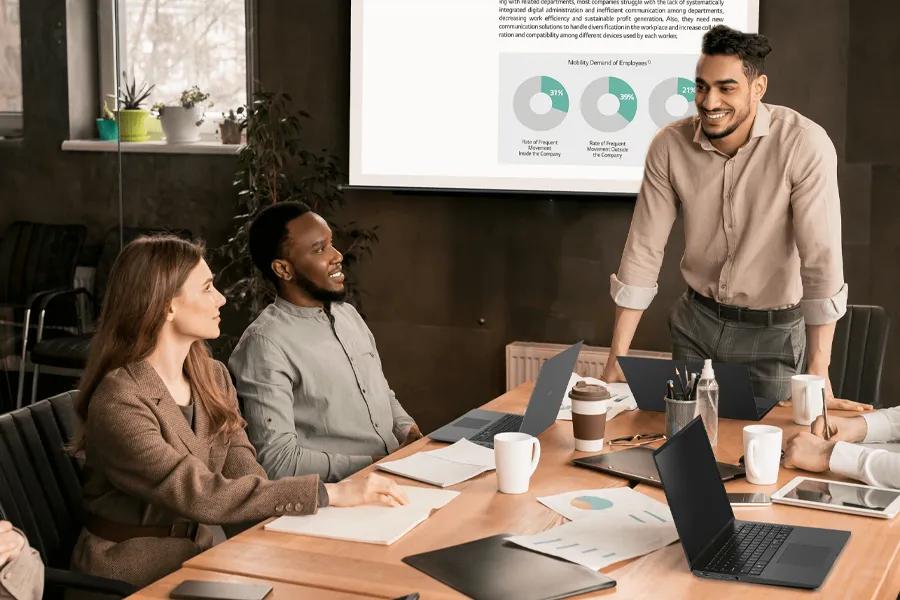 A group of people in a conference room engaged in a meeting with a presentation on the screen. LG gram laptops are on the conference table.