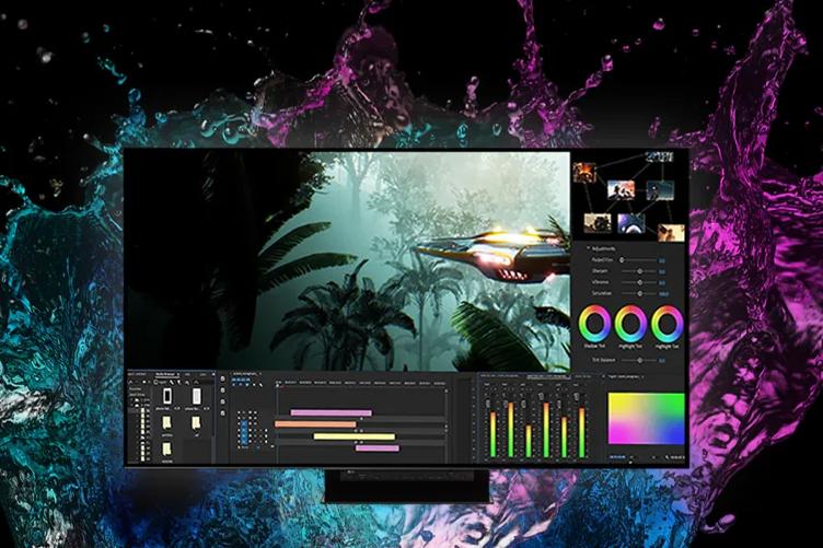 An LG OLED Pro display with video editing software displayed on its screen. Colorful blue, teal, and purple splashes behind it echo the vivid colors on the screen. 