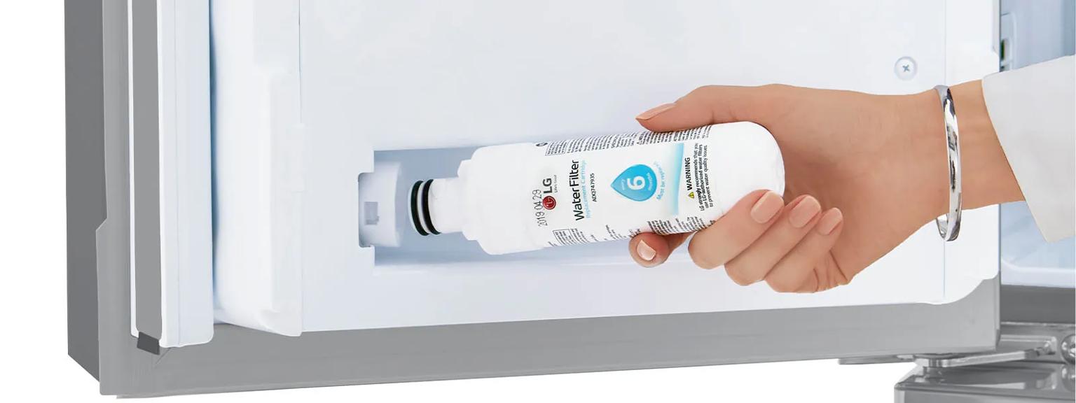 Hand holding refrigerator water filter toward hidden compartment. 