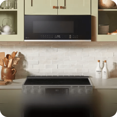 LG low-profile over-the-range microwave mounted above a stove in a light kitchen, with open shelves, tiled backsplash, utensils and bottles.