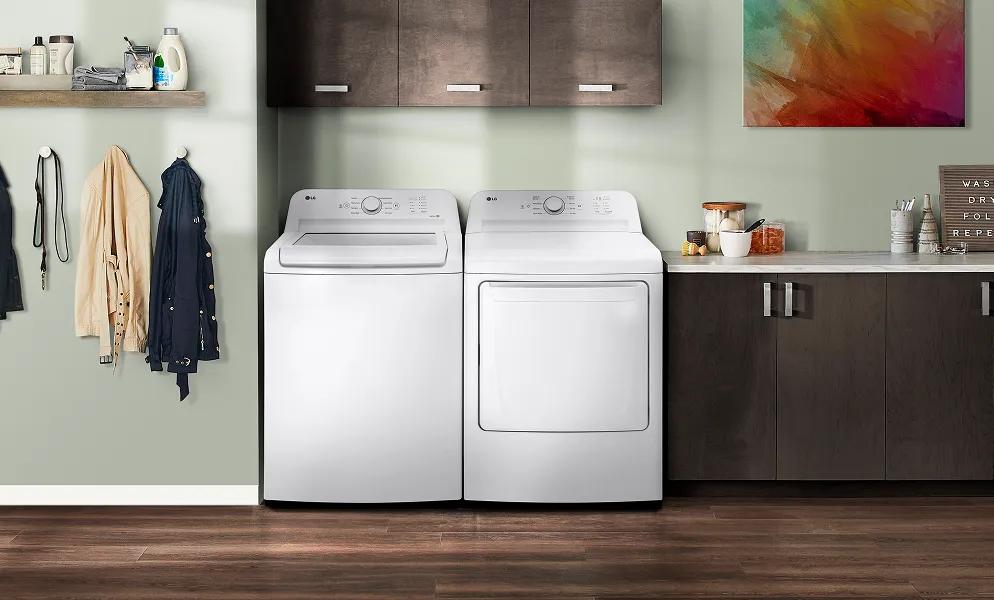 A white LG top load washer and LG front load dryer are in a brightly lit laundry room with wood cabinetry and pistachio-colored walls.