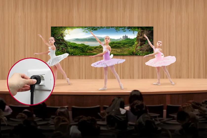 LUPA DVLED on a school stage with a dance recital happening. A cut-out bubble shows a person plugging in LUPA's simple power plug.