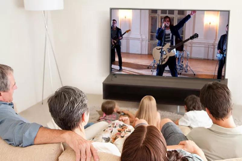 Family of seven gathered in the living room  watching a movie TV screen shows a band performing