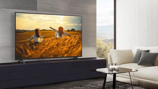 Modern living room with a large TV displaying a bright field scene, a white sofa, and a black glass coffee table.