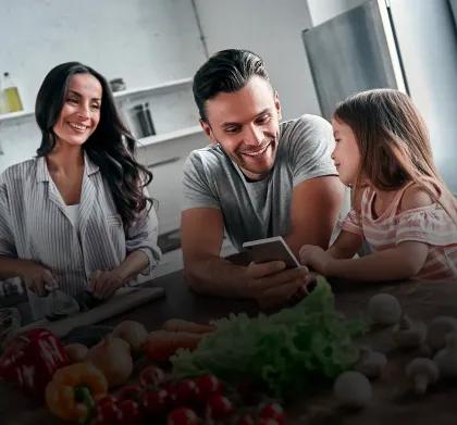 A family preparing food at the kitchen island while looking at the ThinQ recipe on a phone - tablet