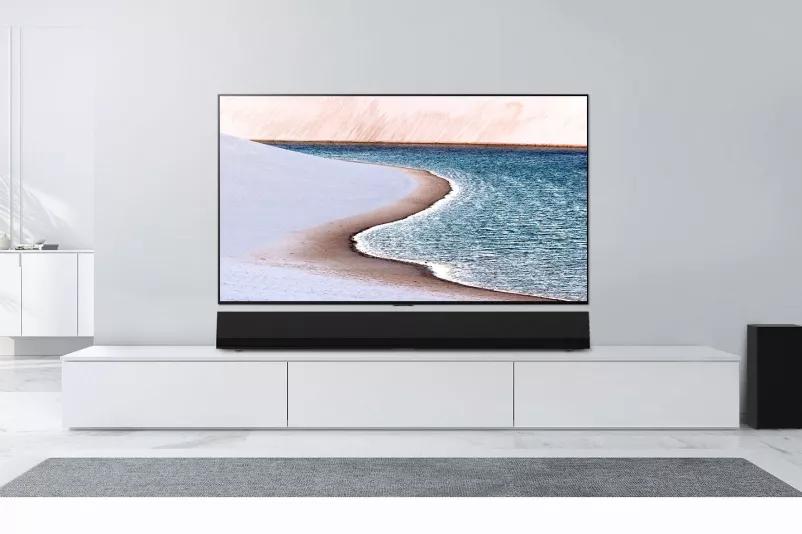 A TV is mounted on light gray wall LG Soundbar is below it on a white cabinet The TV shows a beach