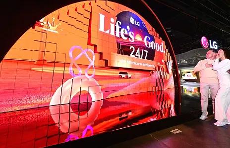 Visitors viewing LG curved LED display showcasing 'Life's Good 24/7' slogan at tech exhibition.