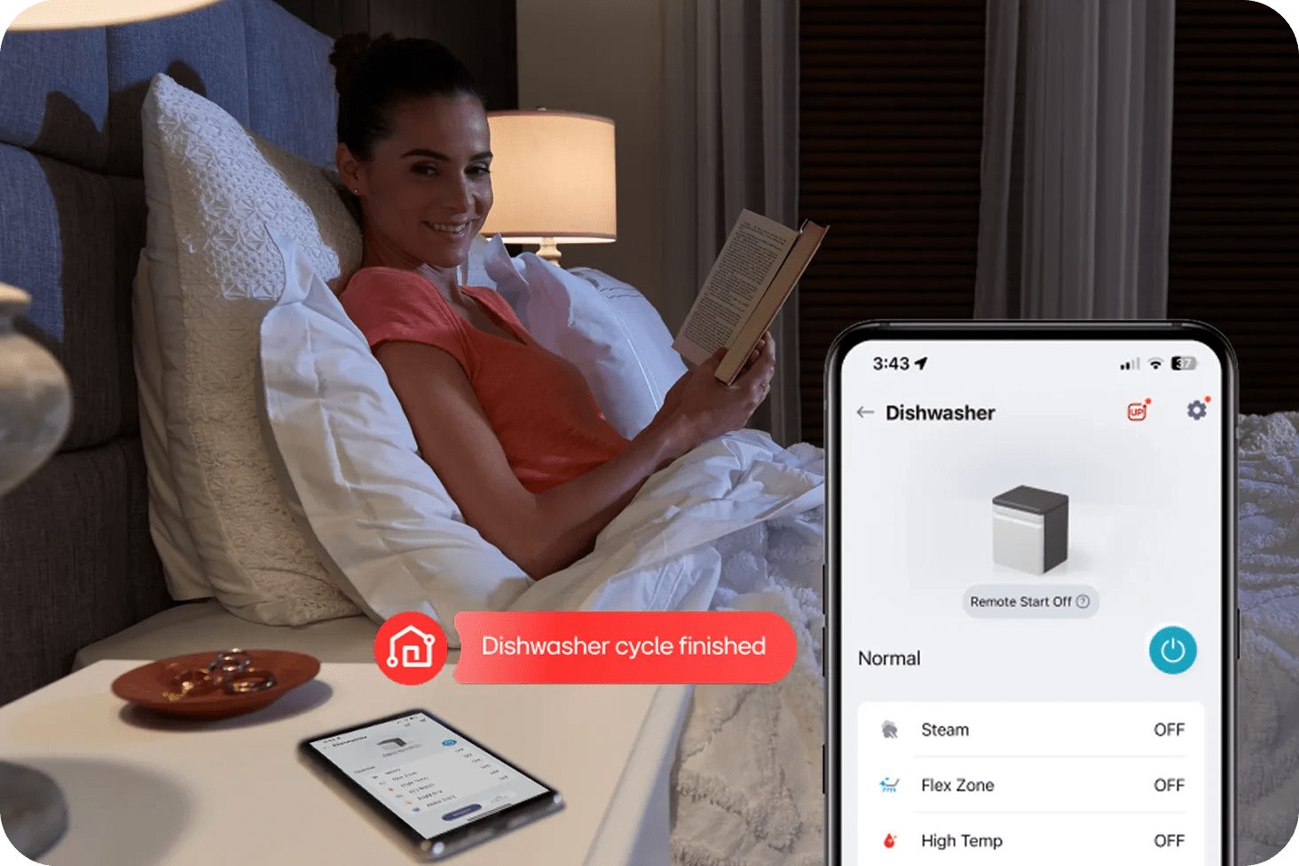 A woman reads a book in bed and looks toward her phone. The phone displays a ThinQ™ notification with the text “Dishwasher cycle finished.””