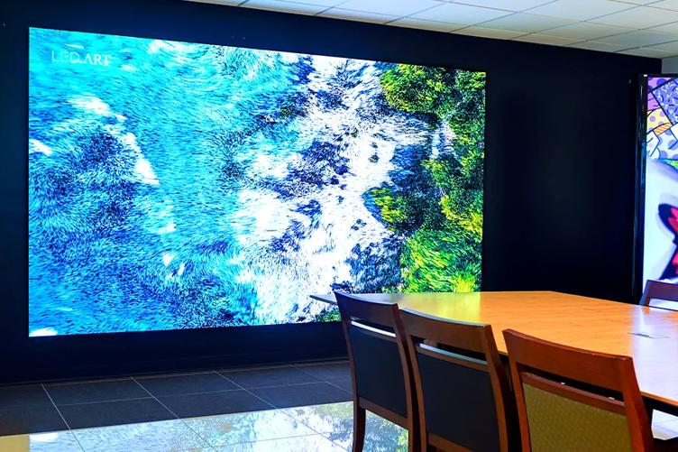 A large Direct View LED display on the wall of the LG Atlanta Business Innovation Center. It shows a vivid aerial scene of an ocean and beach. The light and colors reflect off of the floor and the nearby conference table.