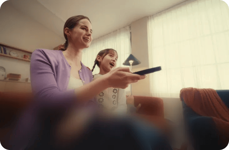 Woman and child smiling while using a remote control to browse streaming content on an LG TV.
