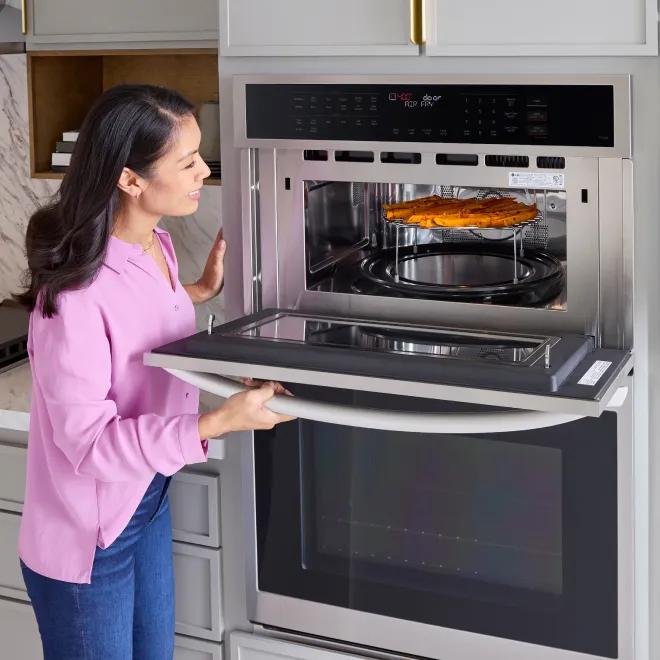  Woman checking on her food in the top oven of an LG wall oven.