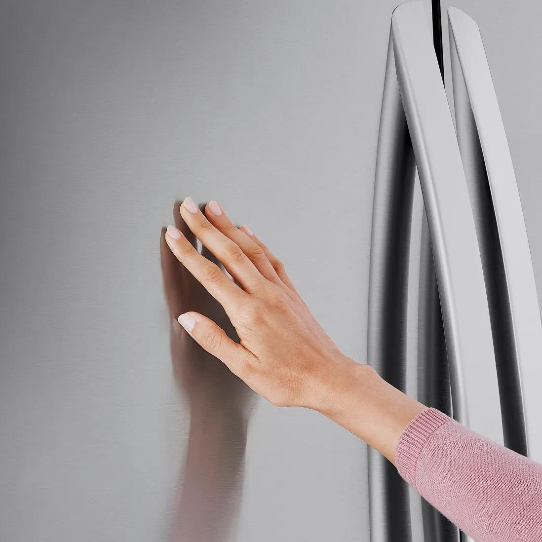 Hand touching the smooth stainless finish on an LG 4-door French door refrigerator, highlighting the PrintProof surface that resists fingerprints and smudges.