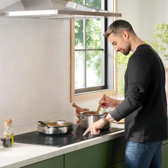 Man standing at the kitchen counter stirring food in a pot on an LG cooktop.