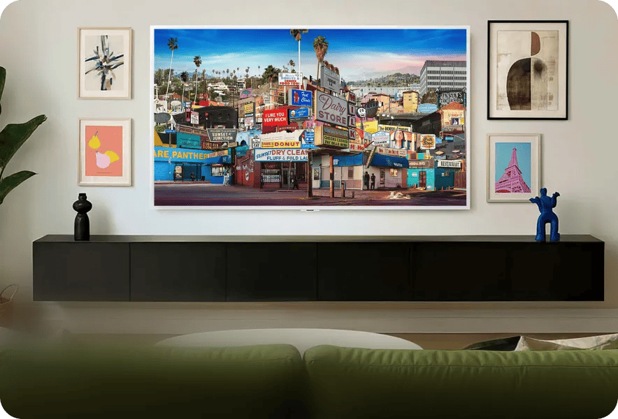 LG TV wall-mounted in a living room displaying colorful street scene artwork, surrounded by framed art prints above a floating media console.