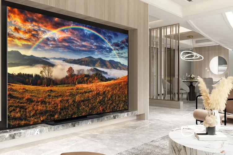 A modern living space with pale chic furnishings and natural-looking lighting. On one wall, a large LG MAGNIT display is mounted. It's showing a vivid image of an autumn forest with a rainbow and sunlit clouds.
