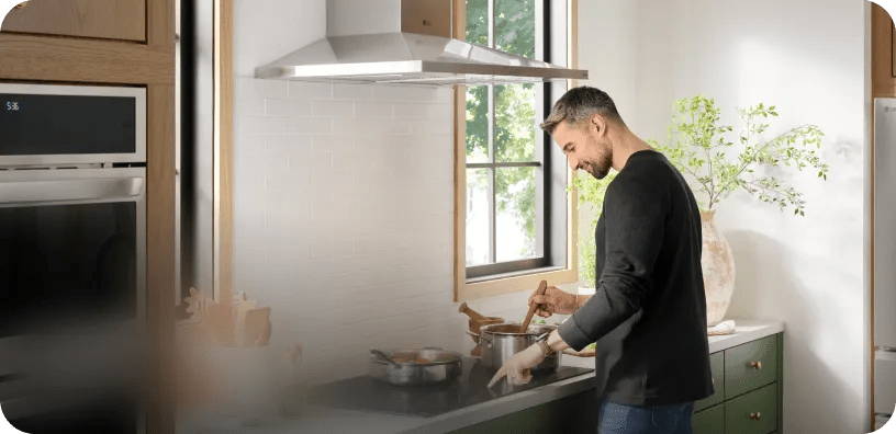 A young man stirs a pot on an LG cooktop underneath an LG hood in a modern kitchen.