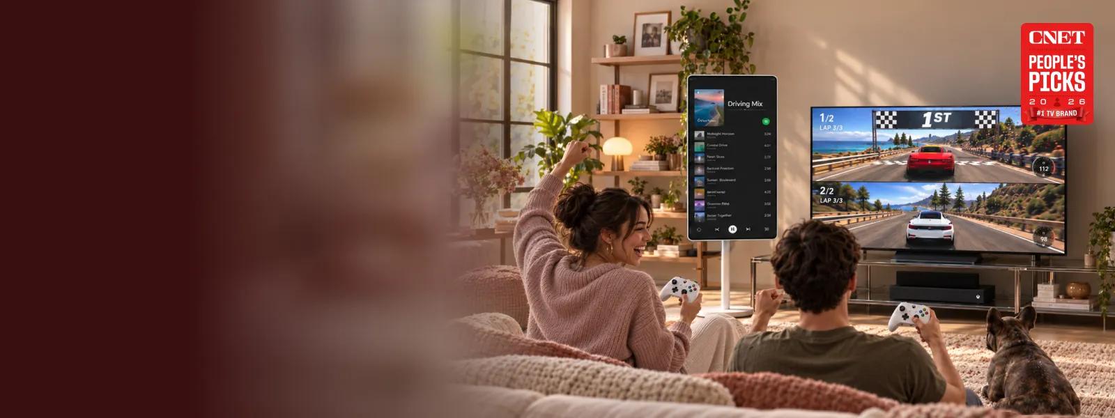 Two people and a dog in a living room playing a split-screen racing game on a large LG TV with Xbox controllers, featuring a vertical smart display to the side and a CNET People's Picks 2026 #1 TV Brand badge.