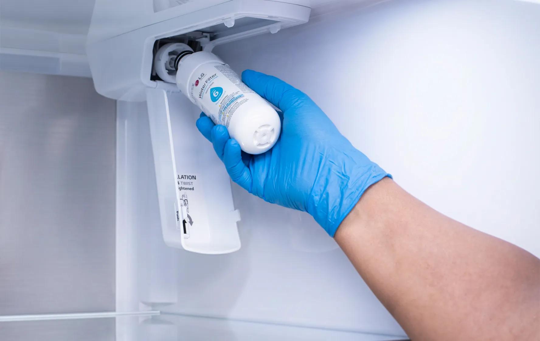 A person wearing a blue protective glove reaching into the upper compartment of an LG refrigerator to install or replace a water filter.