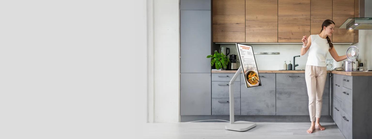 Woman cooking in a modern kitchen beside an LG Smart Monitor Swing that's showing a recipe.