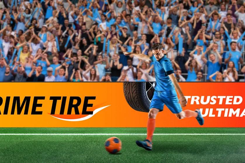 A soccer player in a blue uniform kicking a ball on a field with a cheering crowd and an advertising banner in the background.