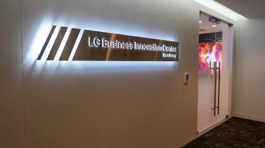 A backlit silver sign reading LG Business Innovation Center New Jersey besides a pair of sleek glass doors. Through the doors a brightly colored DVLED video wall is visible.