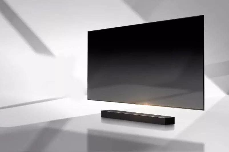 A soundbar and a TV are placed on a white floor and there is a shadow coming from outside right behind