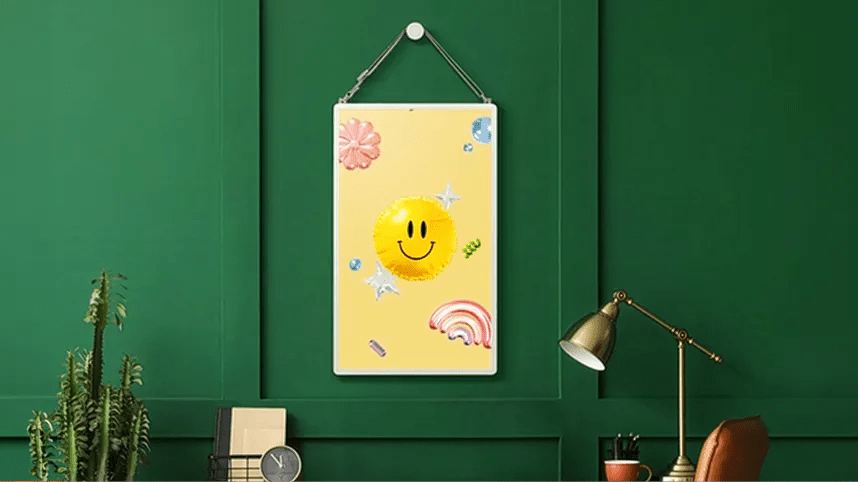 LG StanbyME 2 displayed as a digital picture frame on a dark green wall, showing a smiley face illustration.