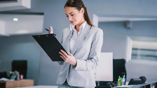 A businesswoman writes something on a clipboard.