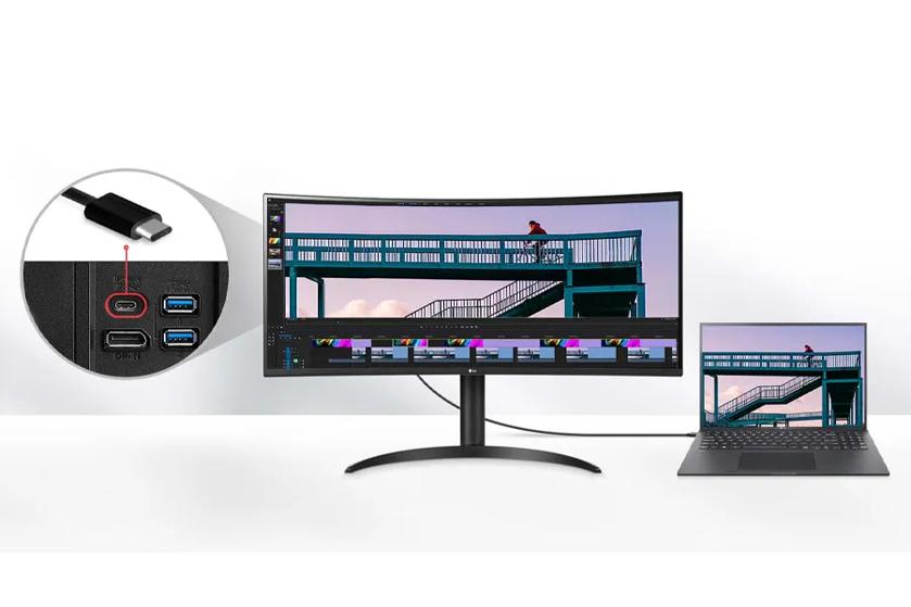 UltraWide monitor connected to a laptop via a USB-C cable, displaying a video editing project with a cyclist on a bridge, featuring a close-up of the USB-C port and highlighting 96W power delivery capability.