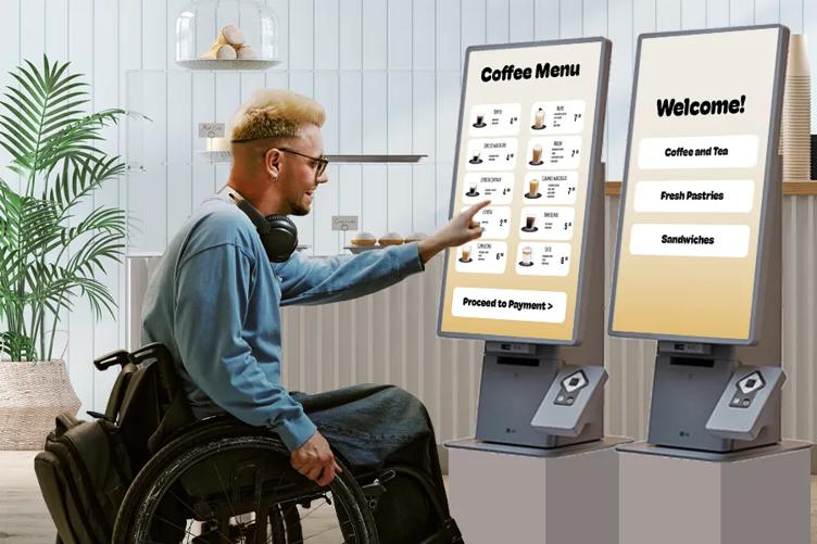 A man in a wheelchair uses an LG Gen 2 Touch Kiosk to order coffee in a chic cafe.