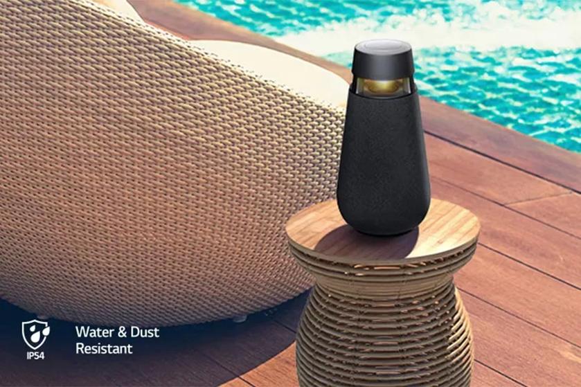 The LG XBOOM 360 Speaker on a table next to a pool on a sunny day.