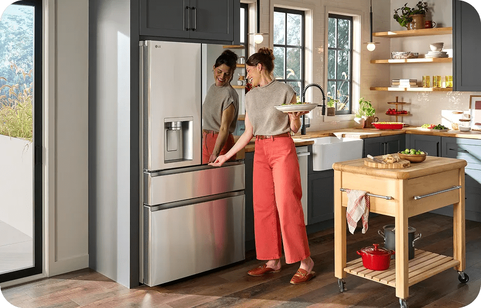 Front view of an installed LG 4-Door French door refrigerator with Mirror InstaView reflecting a woman opening it while holding a salad plate in a bright kitchen.