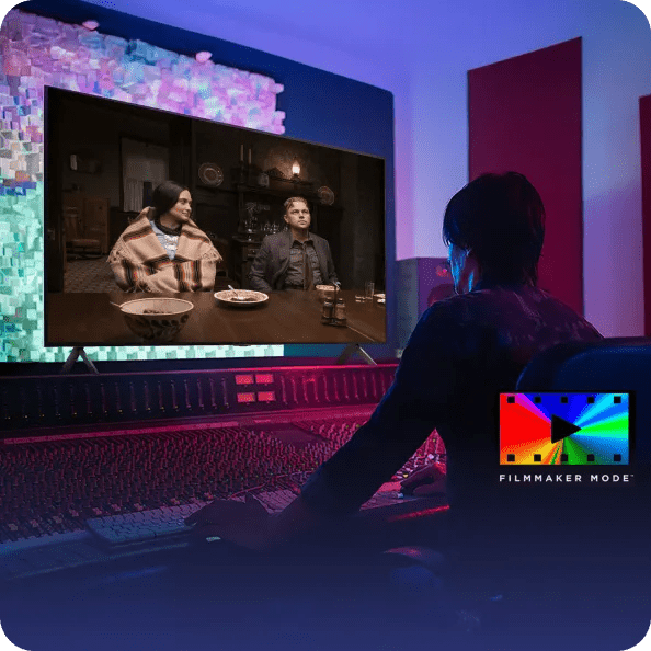 Person working at a video mixing console watches an LG TV showing two people at a dinner table, with “Filmmaker Mode™” text and logo in the corner.