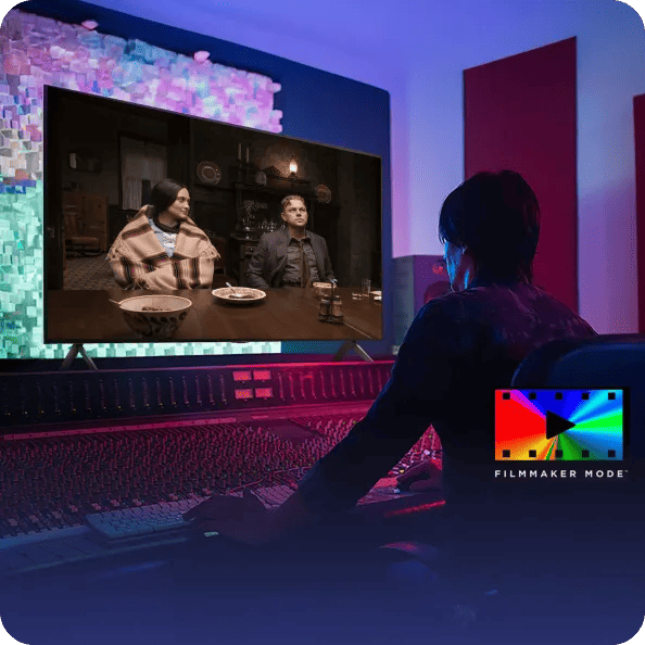 Person working at a video mixing console watches an LG TV showing two people at a dinner table, with “Filmmaker Mode™” text and logo in the corner.