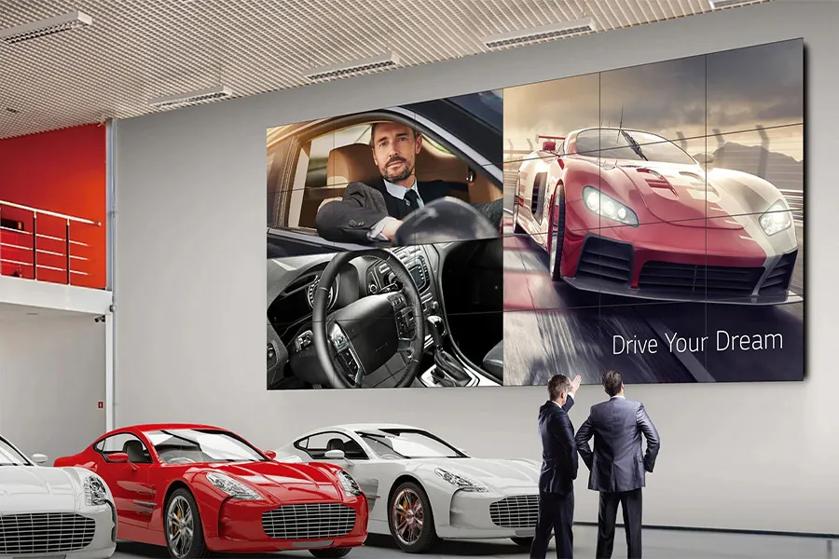 A showroom displaying sports cars with a large multi-panel image on the wall, featuring a man driving, a car's dashboard, a speeding red car, and the phrase "Drive Your Dream."