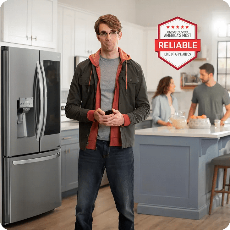 A man standing in a modern kitchen in front of a stainless steel refrigerator, holding a smartphone and looking toward the camera. In the background, a couple stands near a kitchen island with a bowl of oranges and a pitcher. A red and white badge graphic on the right reads: “Brought to you by America’s Most Reliable Line of Appliances.”